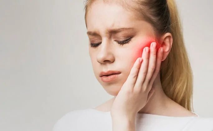 Woman holding her jaw in pain, a common sign of TMJ problems