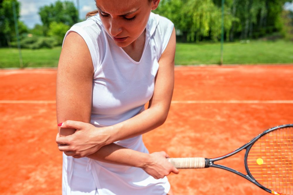 Tennis player holding the outside of her painful elbow, a common sign of tennis elbow